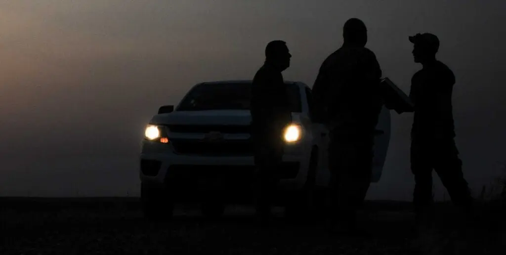 Two men standing next to a car on the side of a road.