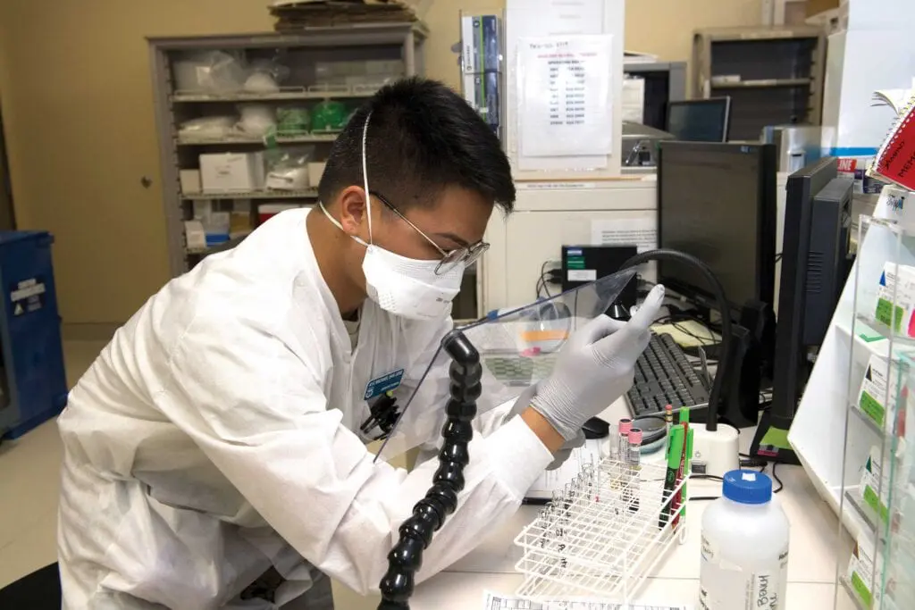 A man in white lab coat and mask working on a computer.