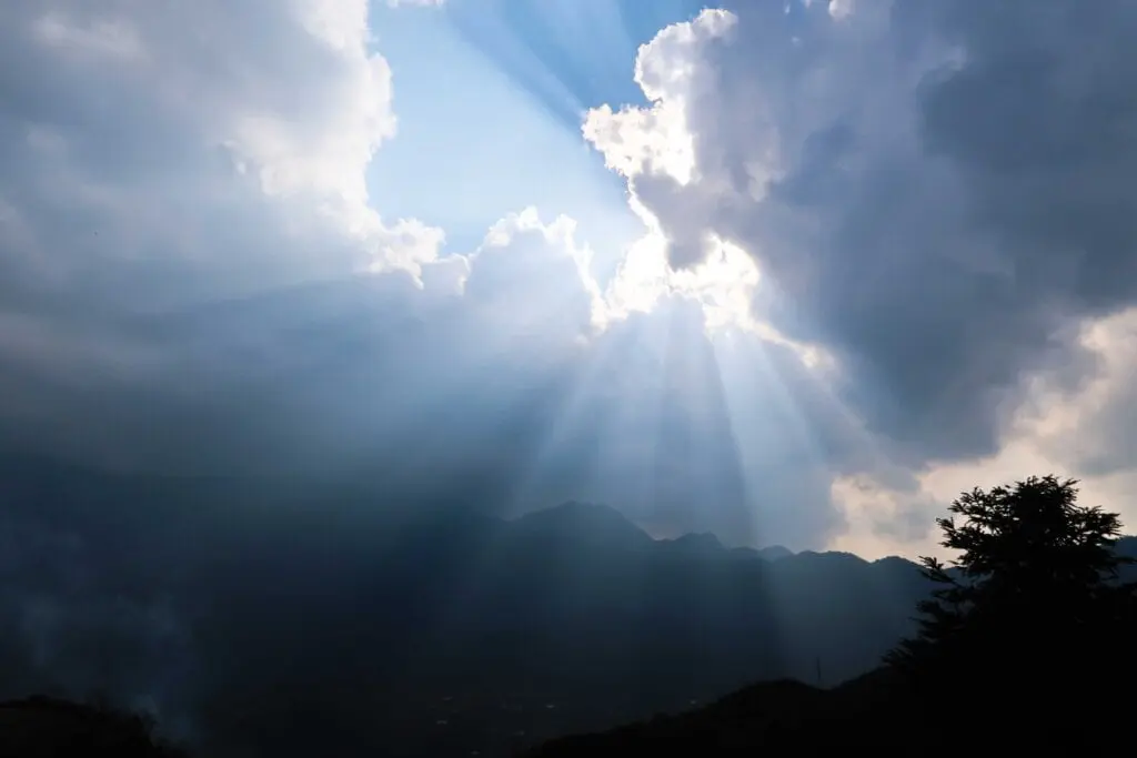 A sun beam shining through the clouds on top of a mountain.