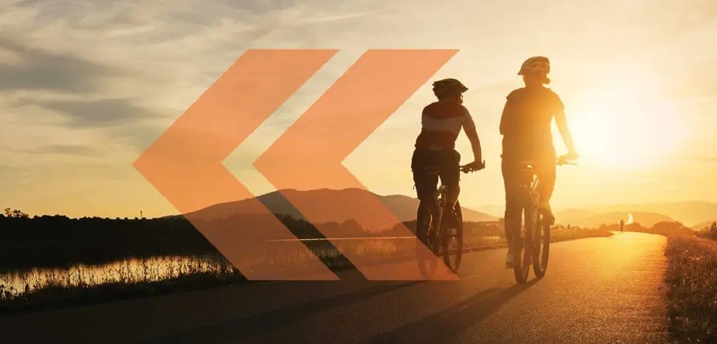Two people riding bikes on a road at sunset.