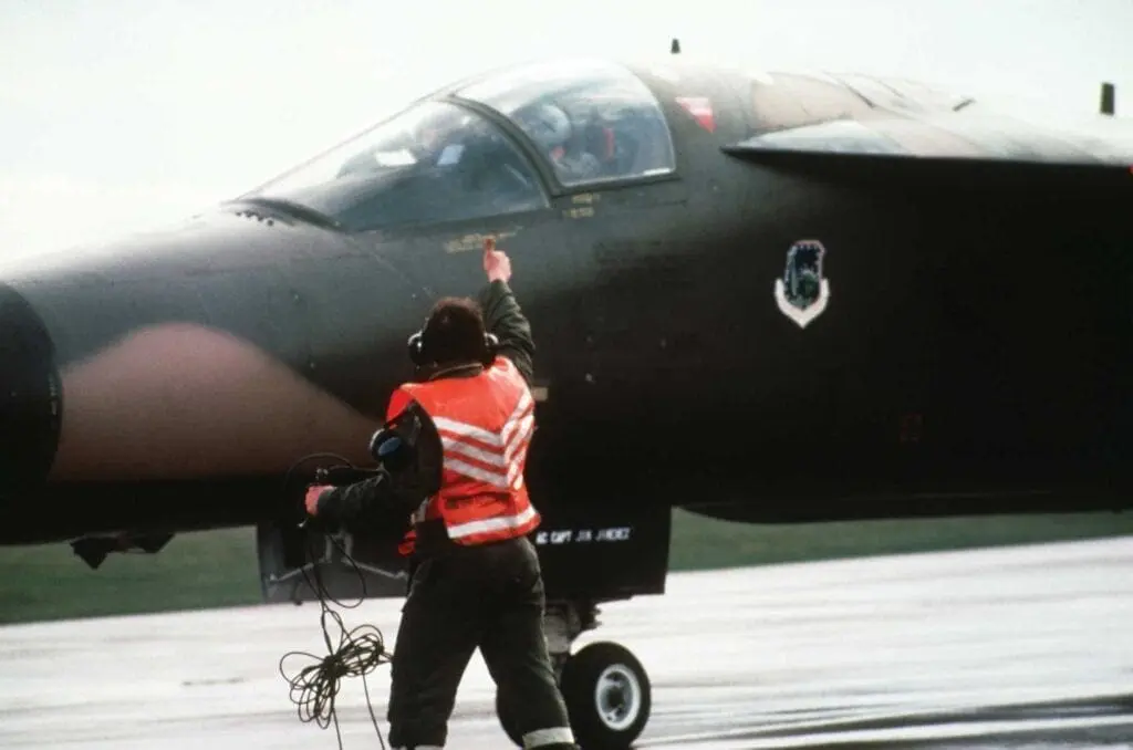 A man in an orange vest standing next to a black jet.