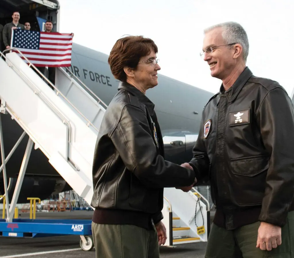 A man and woman shaking hands near an airplane.