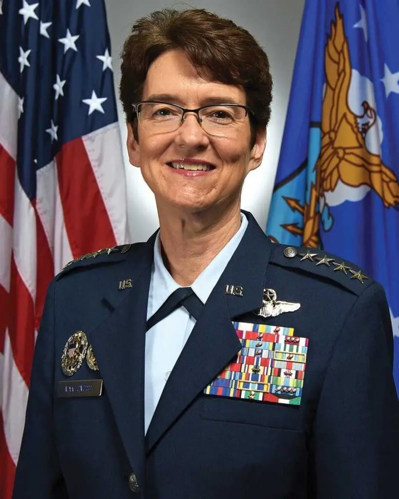 A woman in military uniform standing next to flags.