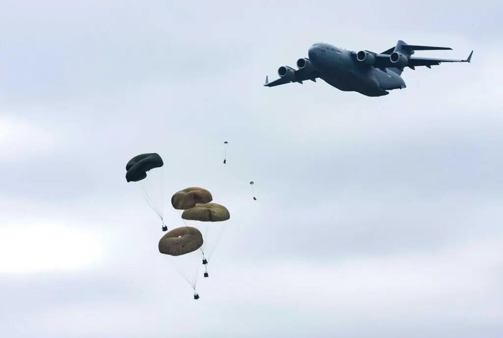A large military plane flying in the sky with parachutes.
