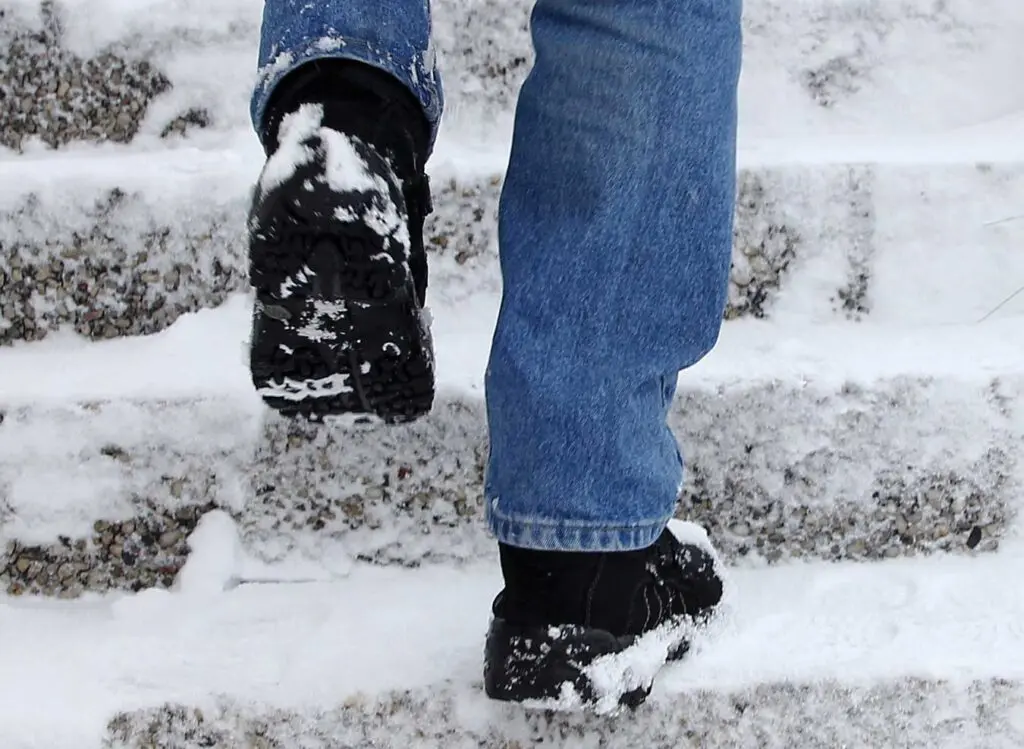 A person walking in the snow wearing black shoes.