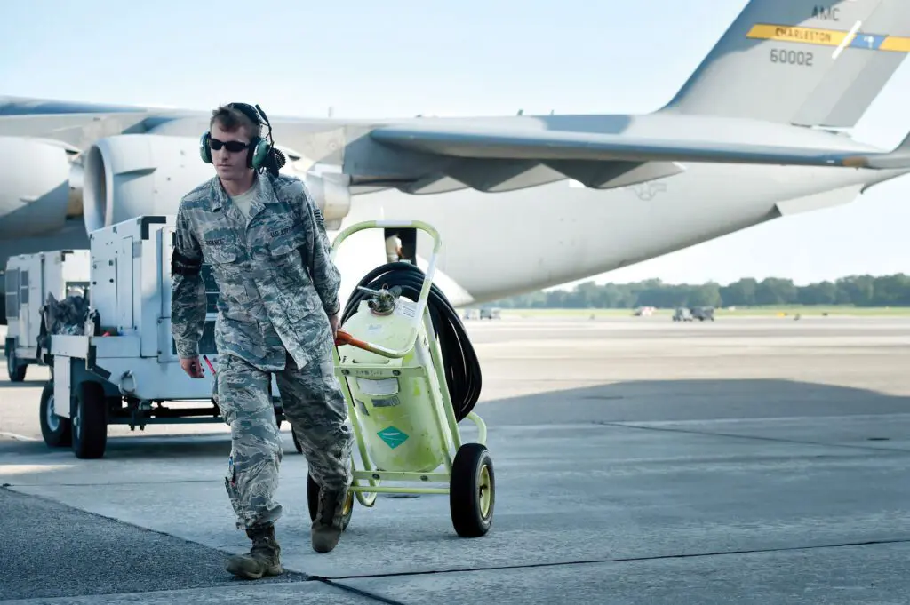 A man in fatigues walking with luggage on the ground.