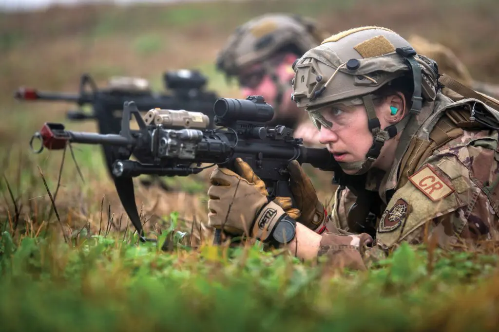 Two soldiers are laying in the grass with guns.