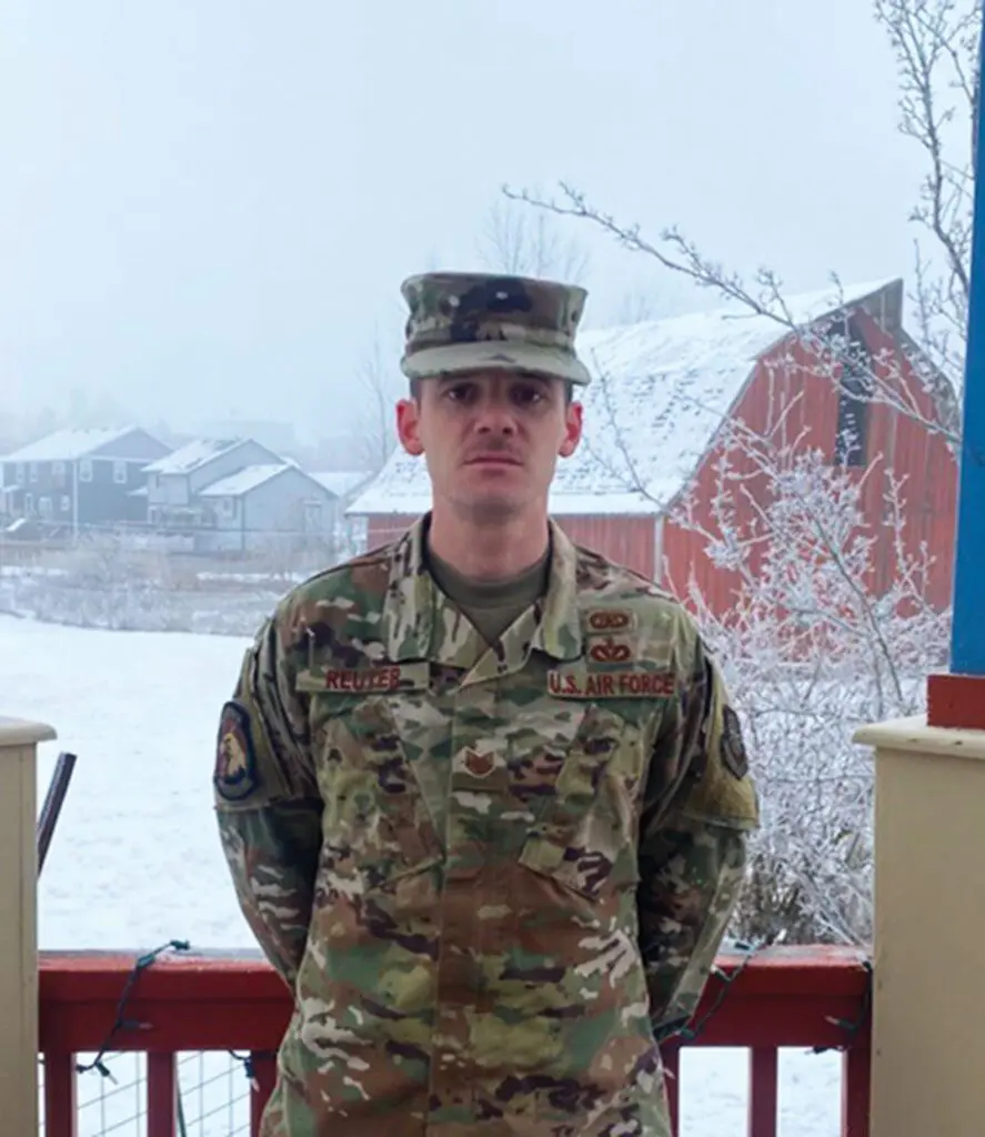 A soldier standing in front of some snow covered trees.