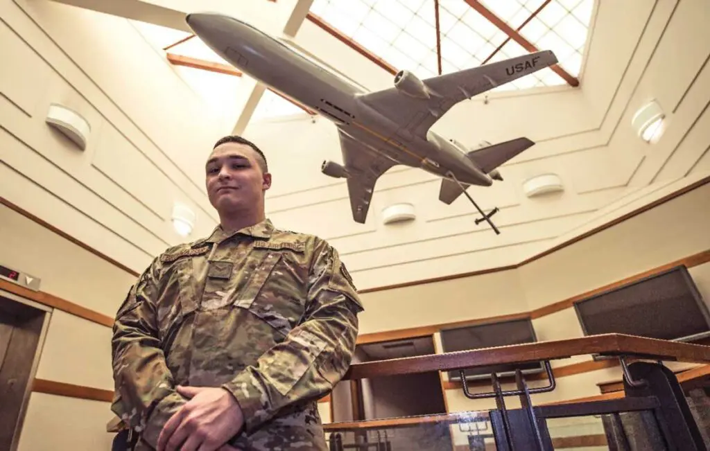 A man in military fatigues standing under an airplane model.