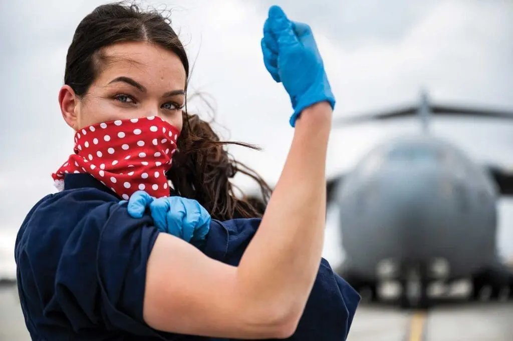 A woman wearing gloves and a mask is holding her arm up.