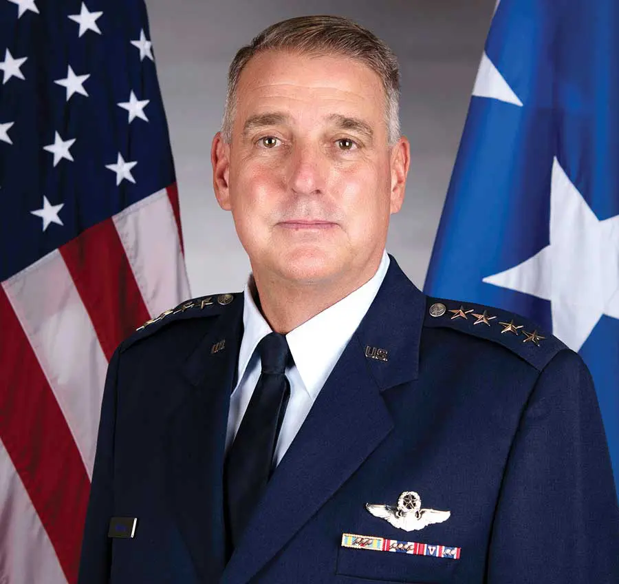 A man in military uniform standing next to two flags.