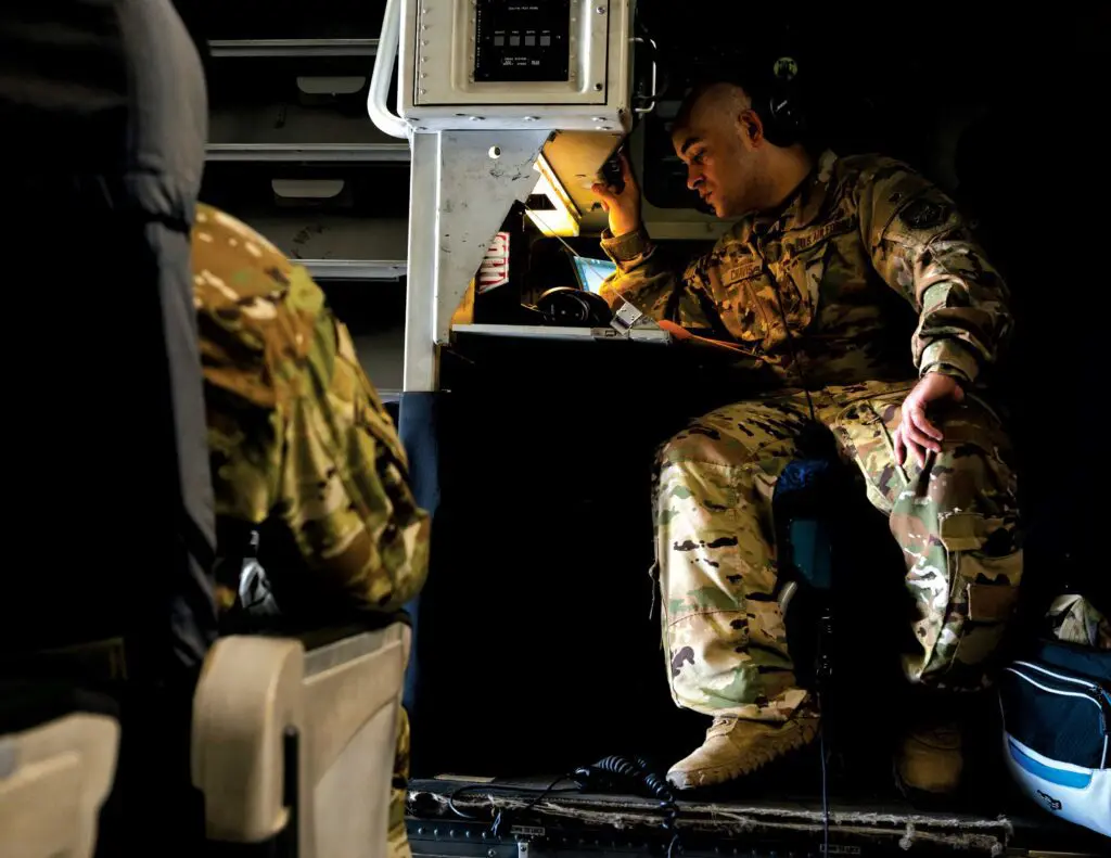 A soldier sitting on the ground in front of an airplane.