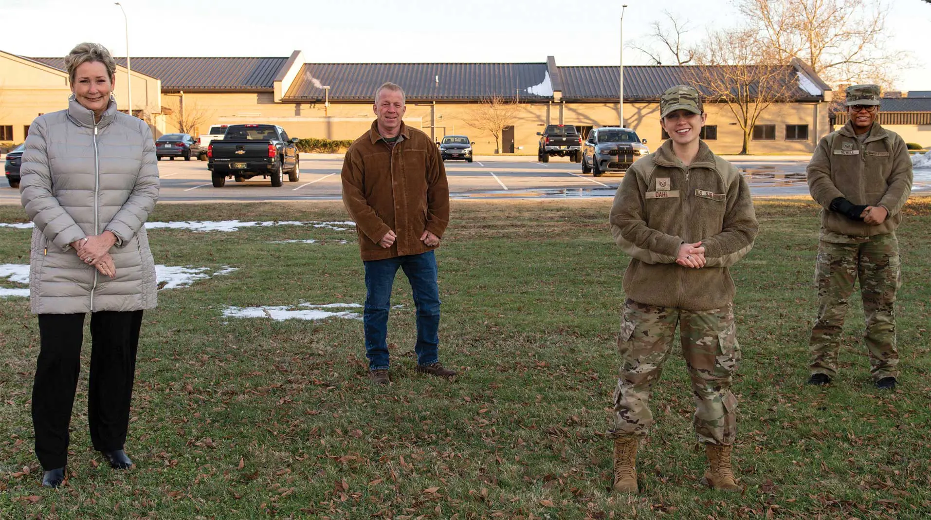 Two men standing in a field with cars parked behind them.