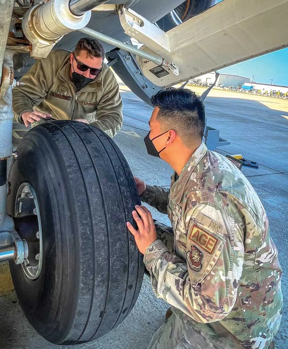 A man in military fatigues and a person in camouflage are working on an airplane tire.