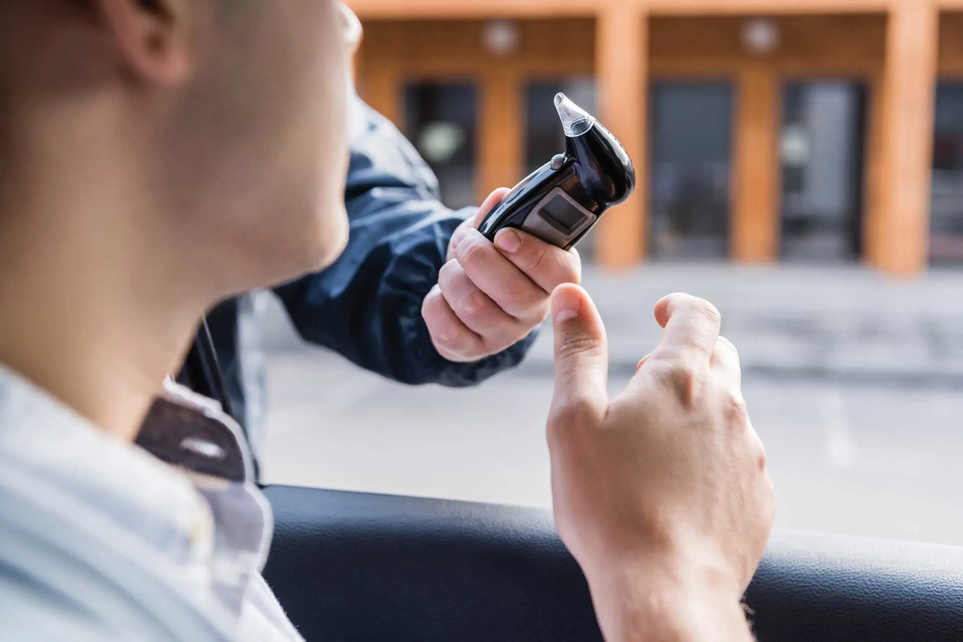 A man in the back of a car holding up his cell phone.