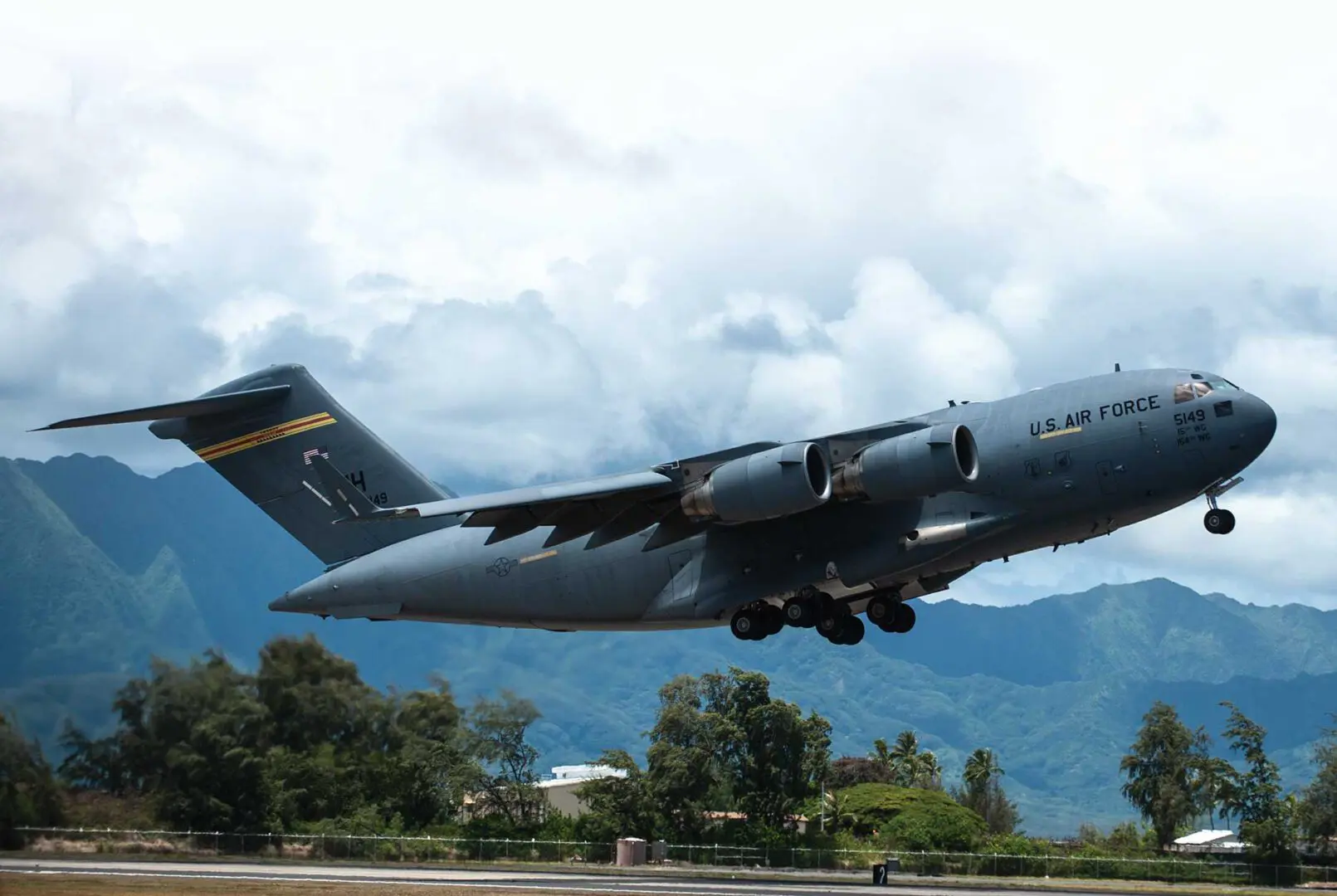 A large military plane flying over the ground.