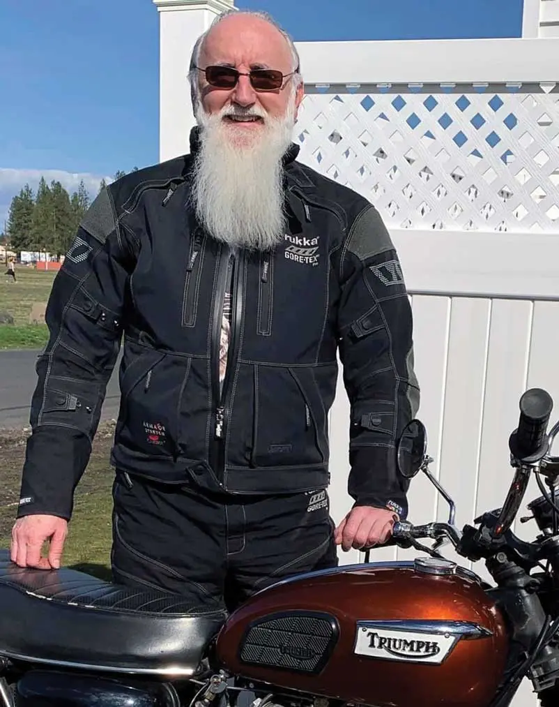 A man with long white beard standing next to his motorcycle.