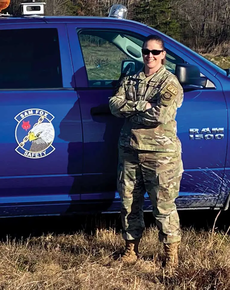 A woman in military fatigues standing next to a truck.