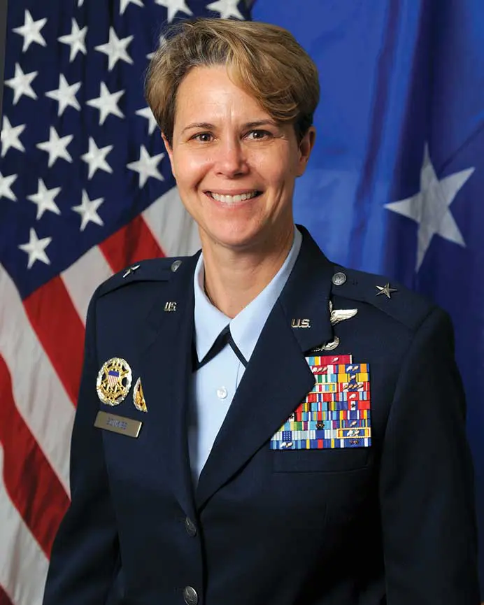 A woman in military uniform standing next to an american flag.