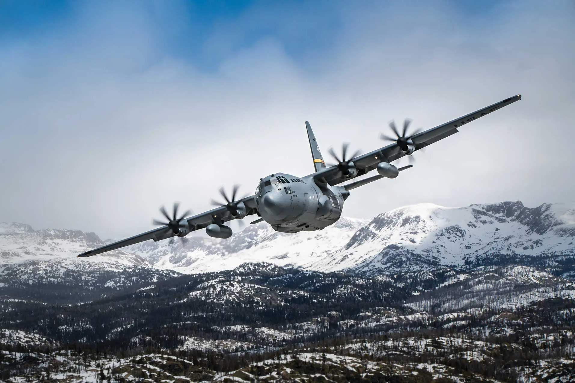 A large airplane flying over the mountains in the snow.