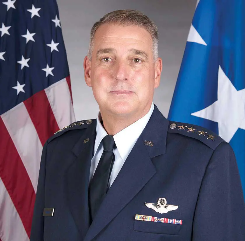 A man in military uniform standing next to flags.