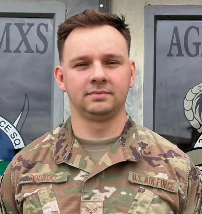 A man in military fatigues standing next to a building.