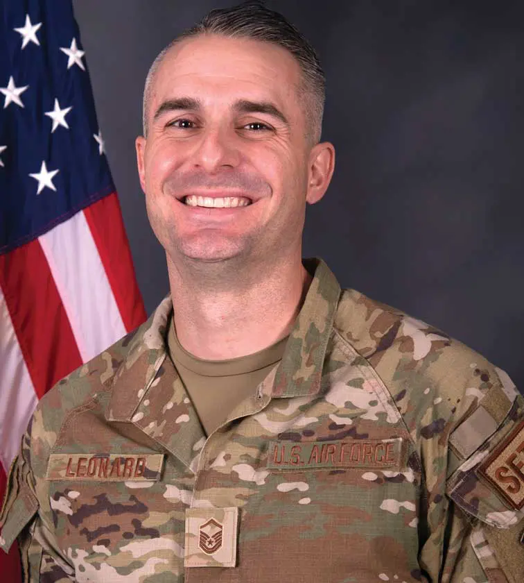 A man in military uniform with an american flag behind him.