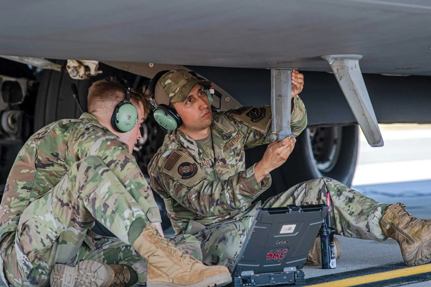 Two soldiers working on a laptop in the back of an aircraft.