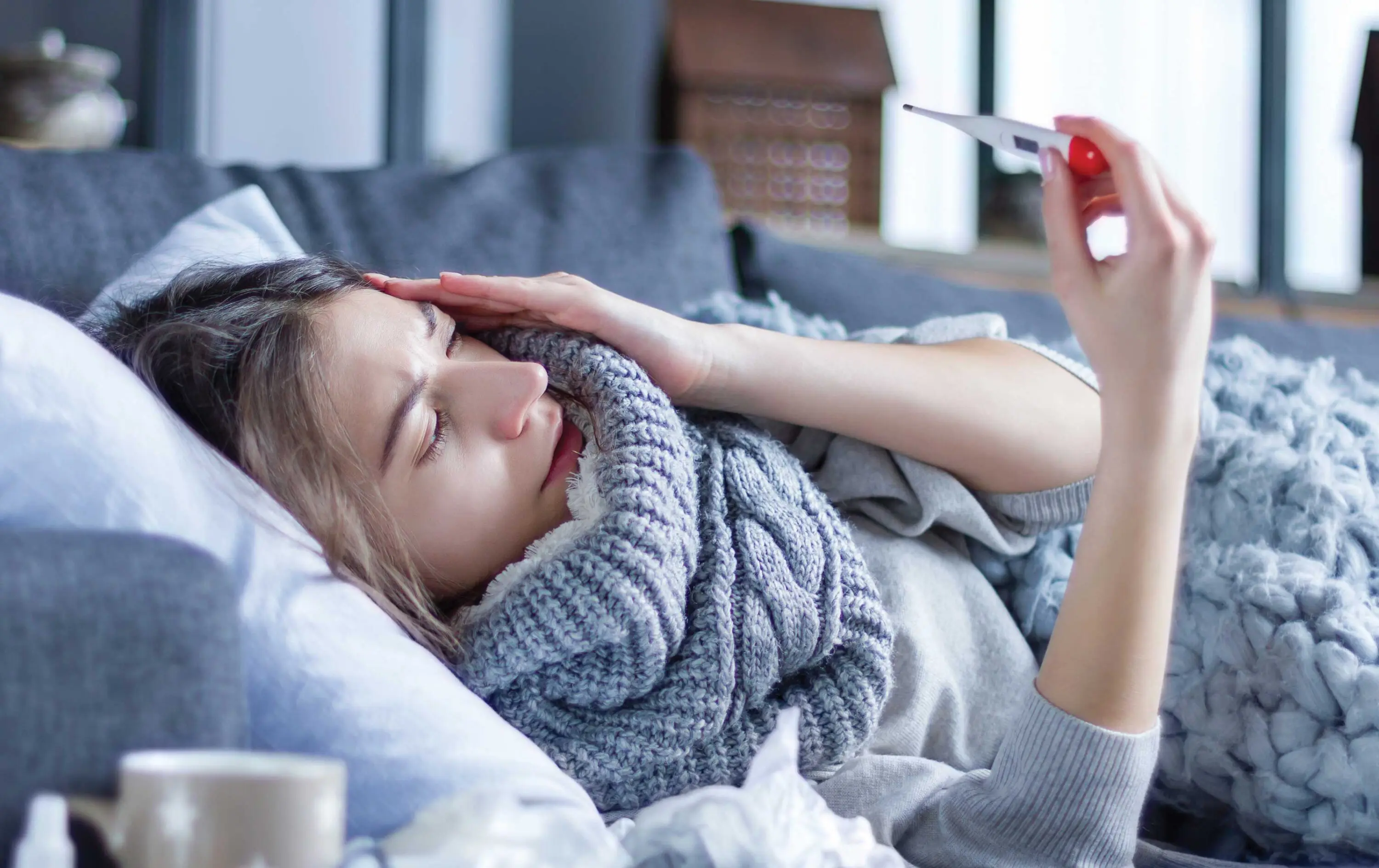 Person on the couch not feeling well looking at a thermometer.