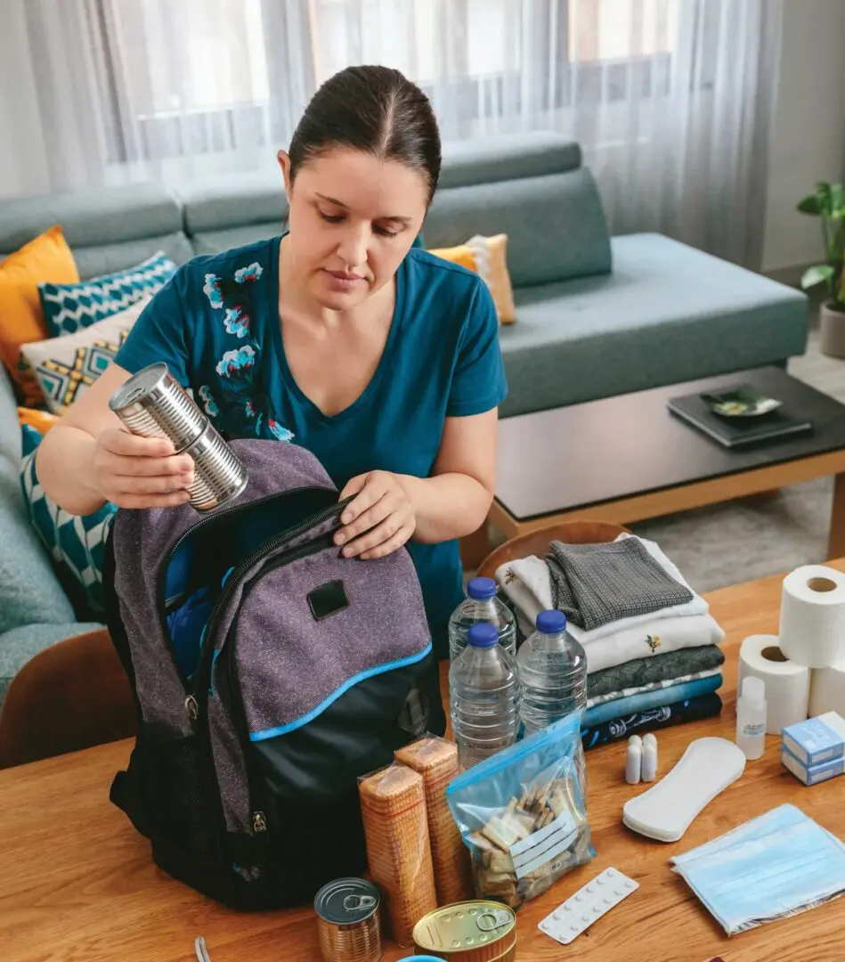 Person packs a backpack of safety supplies, water, can food, bandages, few clothes, etc.