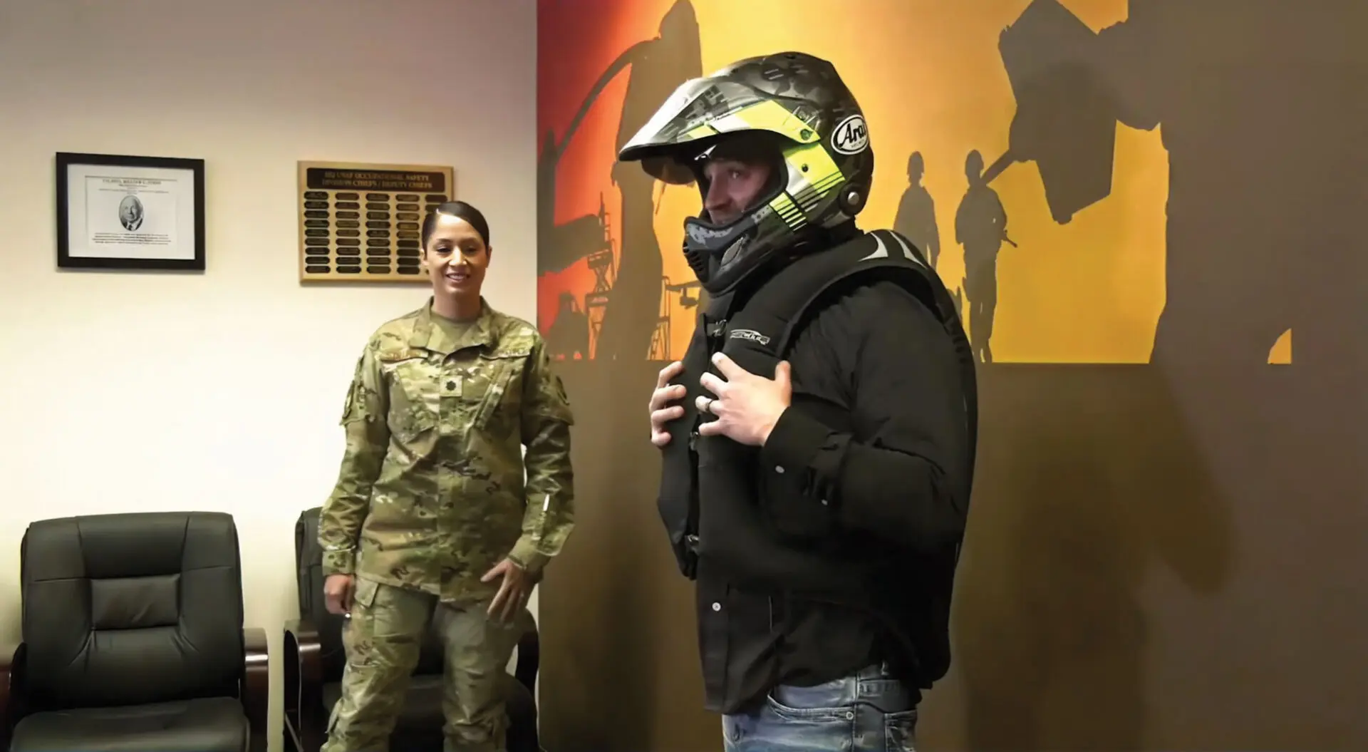 Lt Col Heidi Stallings looks on as Mr. Dave Brandt, wearing a motorcycle helmet and motorcycle airbag vest, demonstrates how quickly the vest inflates when a ball-bearing rip cord is activated.