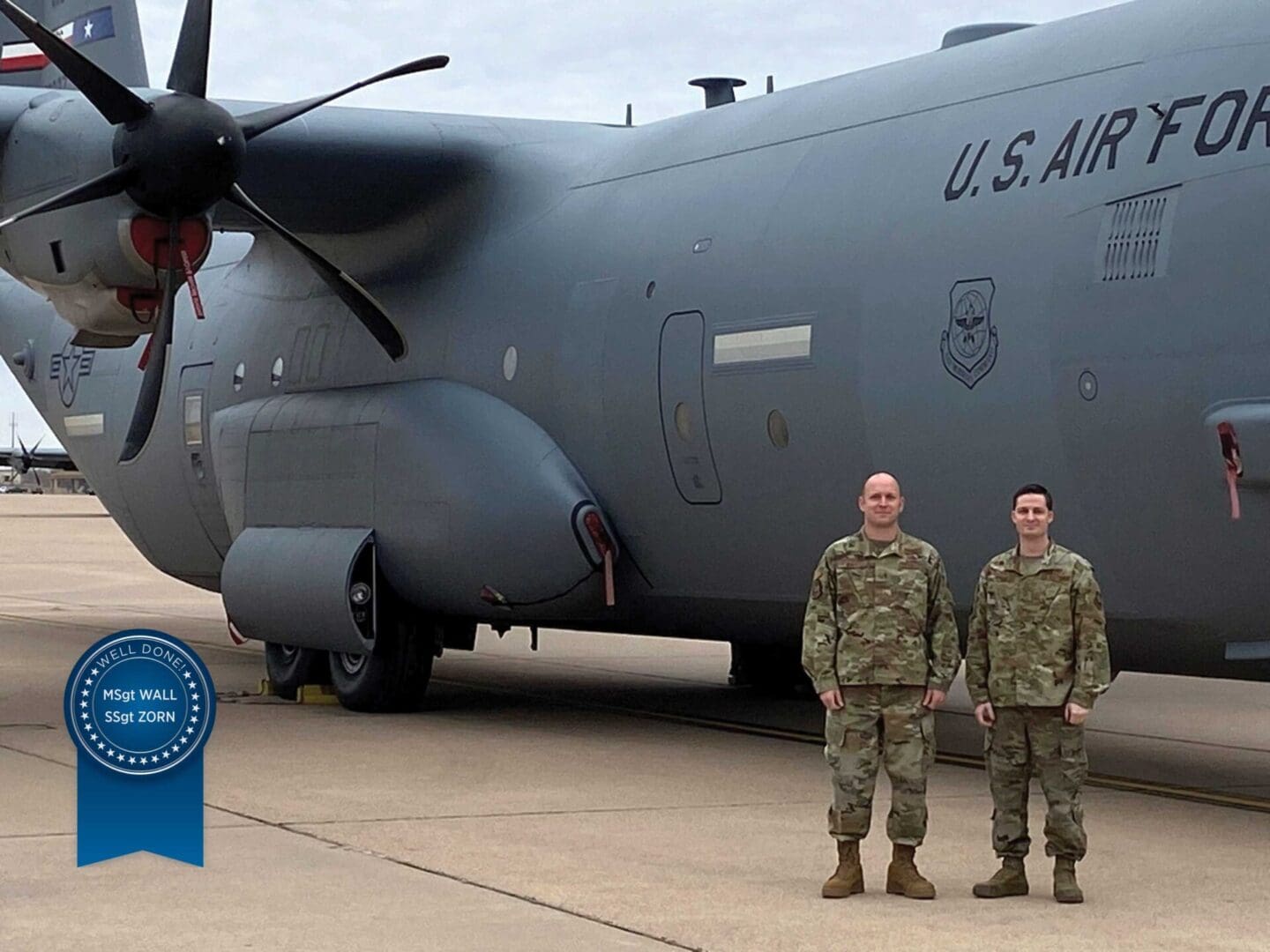 Two men in military uniforms standing next to a large plane.