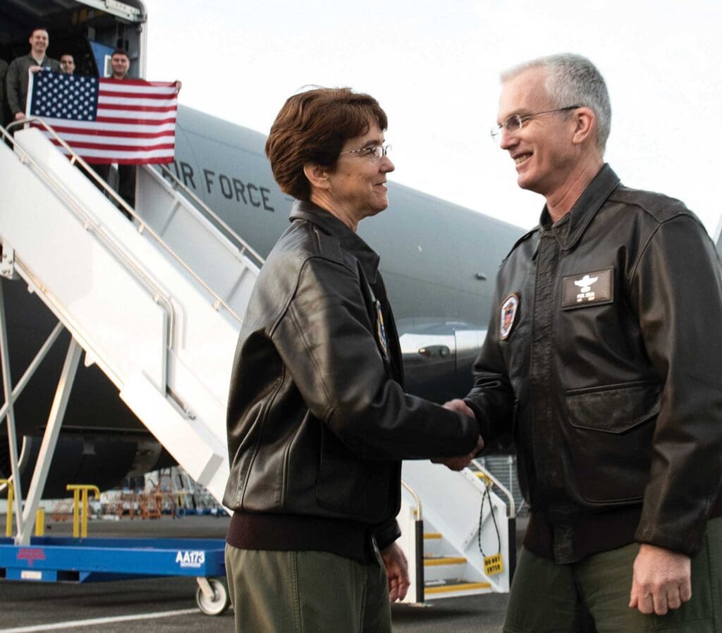 A man and woman shaking hands near an airplane.