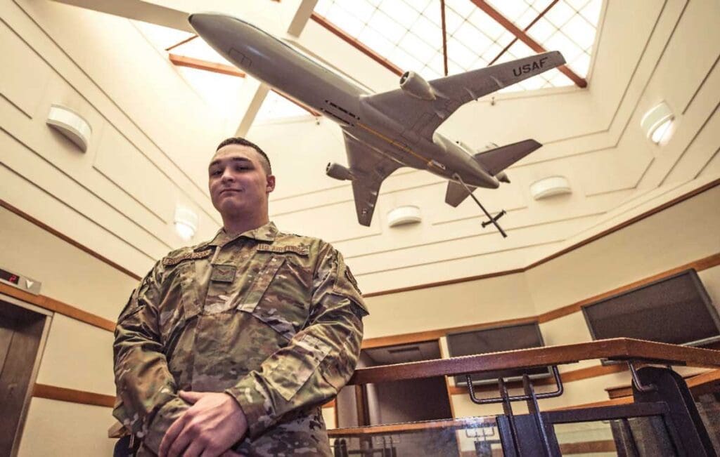 A man in military fatigues standing under an airplane model.