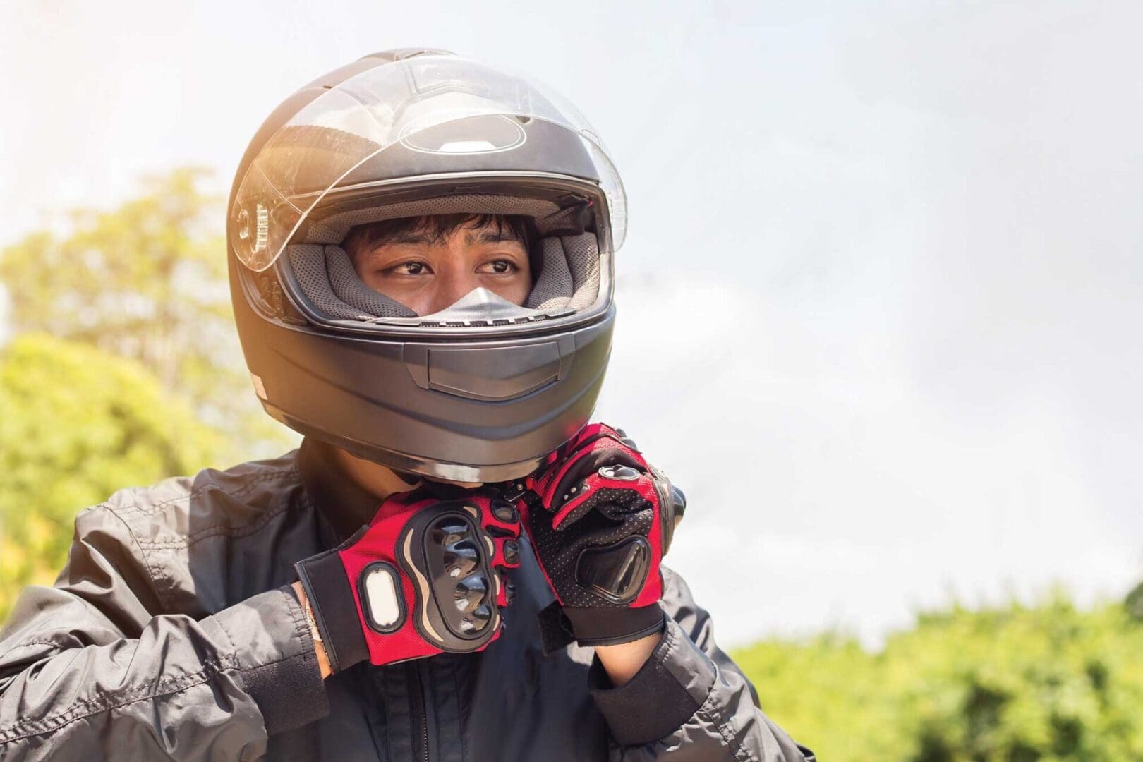 A person in black jacket holding helmet and gloves.