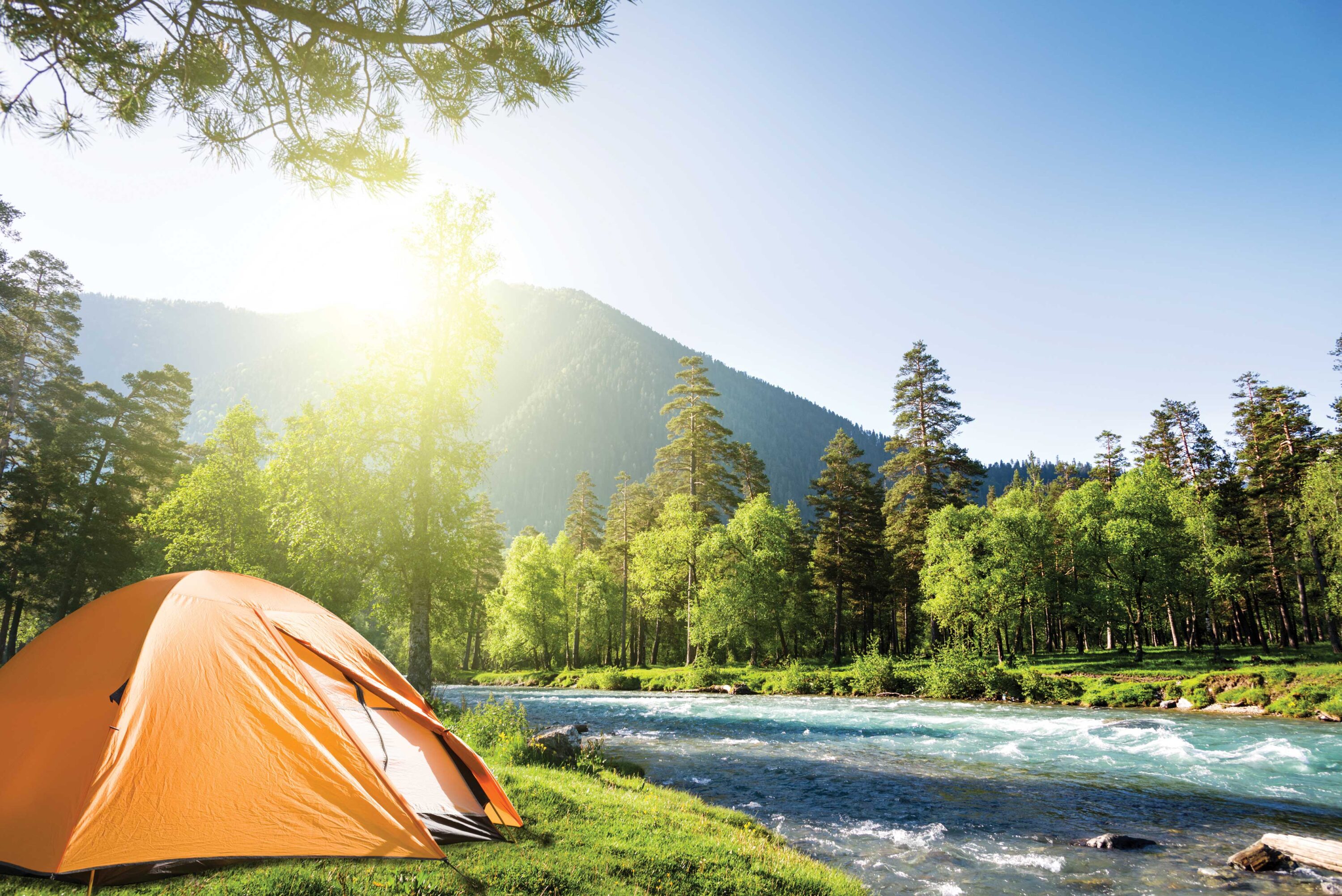 Brightly colored tent sets next to a swiftly flowing body of water lined with bright green trees.