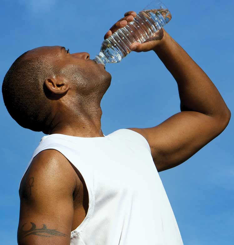 Man drinking a bottle of water against a deep blue sky.