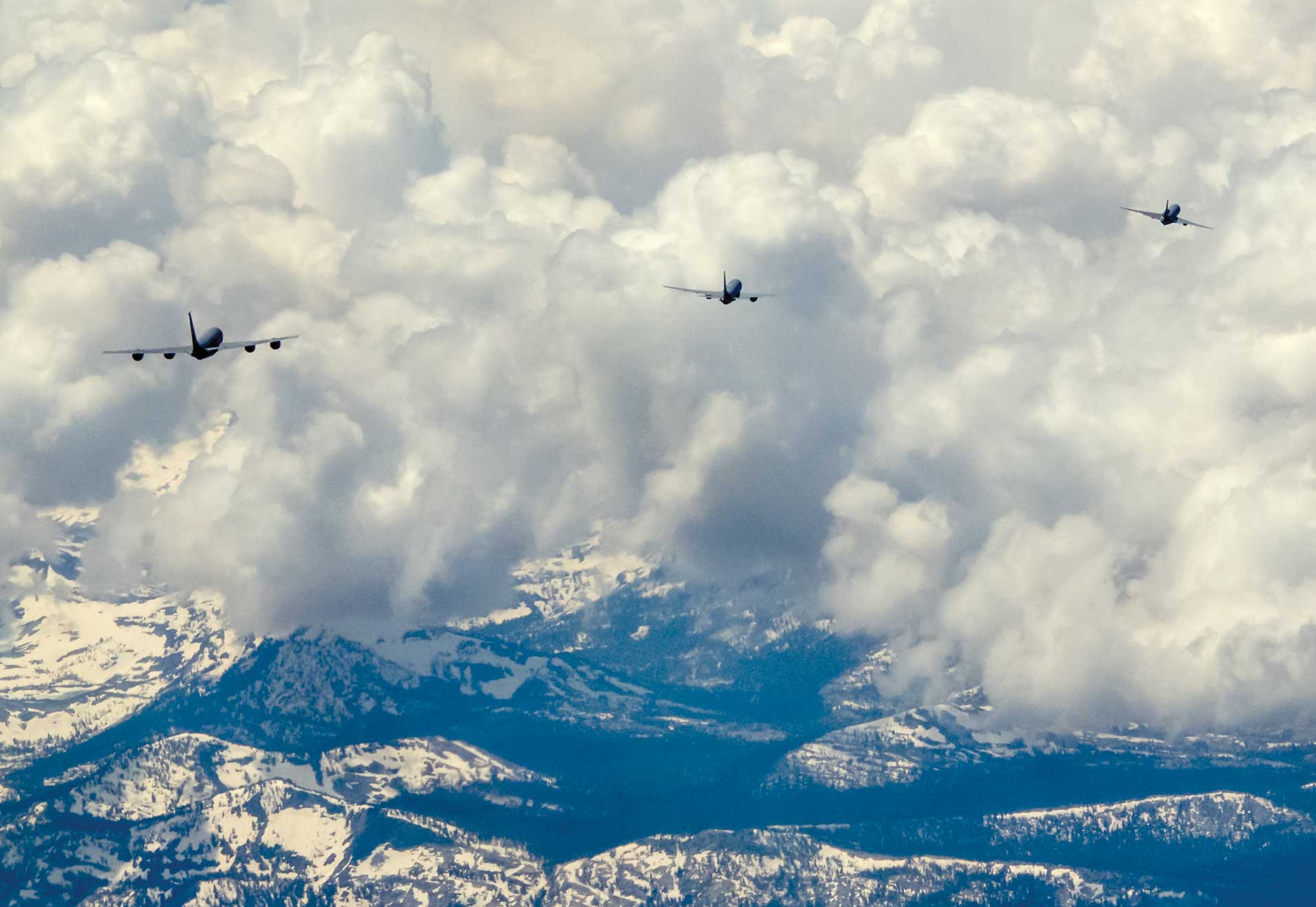 A group of planes flying in the sky above some mountains