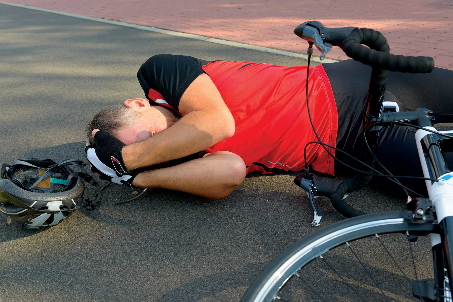 Injured cyclist lying on the ground holding his head.