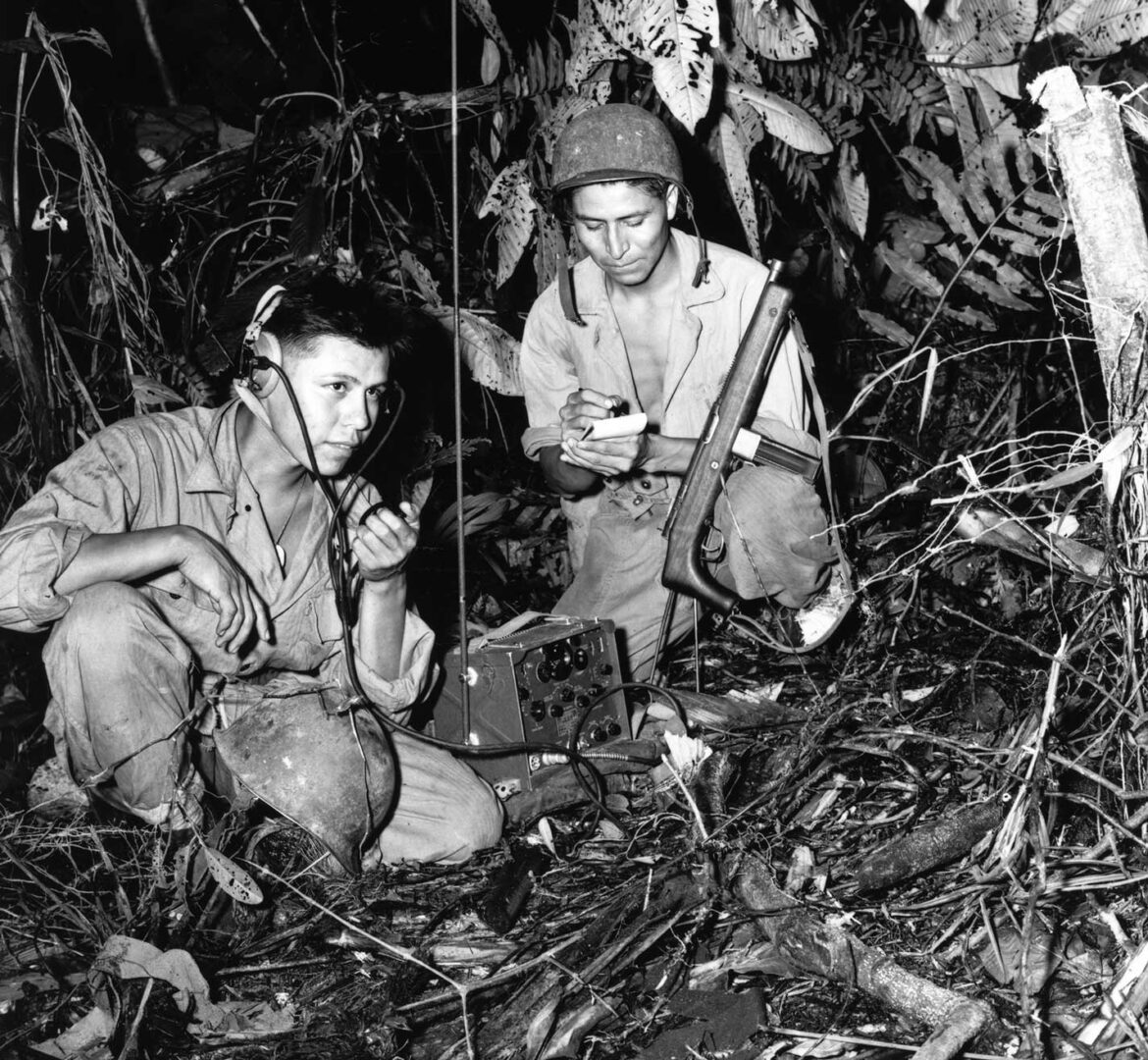 Cpl Henry Blake Jr., (left) and PFC George H. Kirk, Navajo Indians serving with a Marine Signal Unit, operate a portable radio set in a clearing in the dense jungle close behind the frontlines. Bougainville, December, 1943.