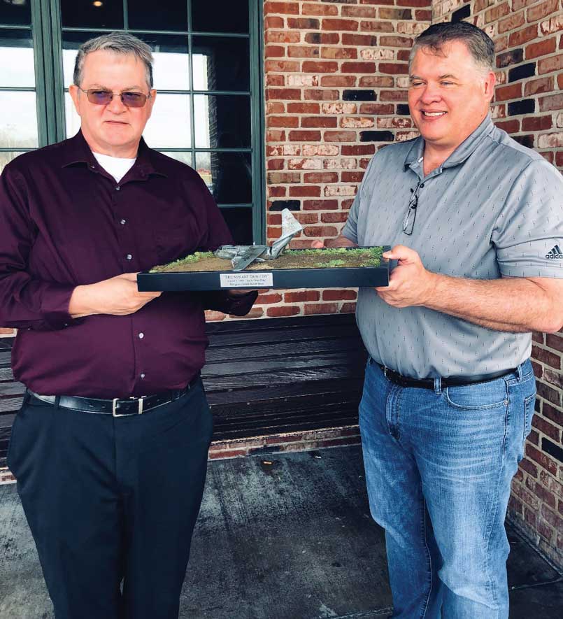 Two men holding a tray of food in front of brick wall.