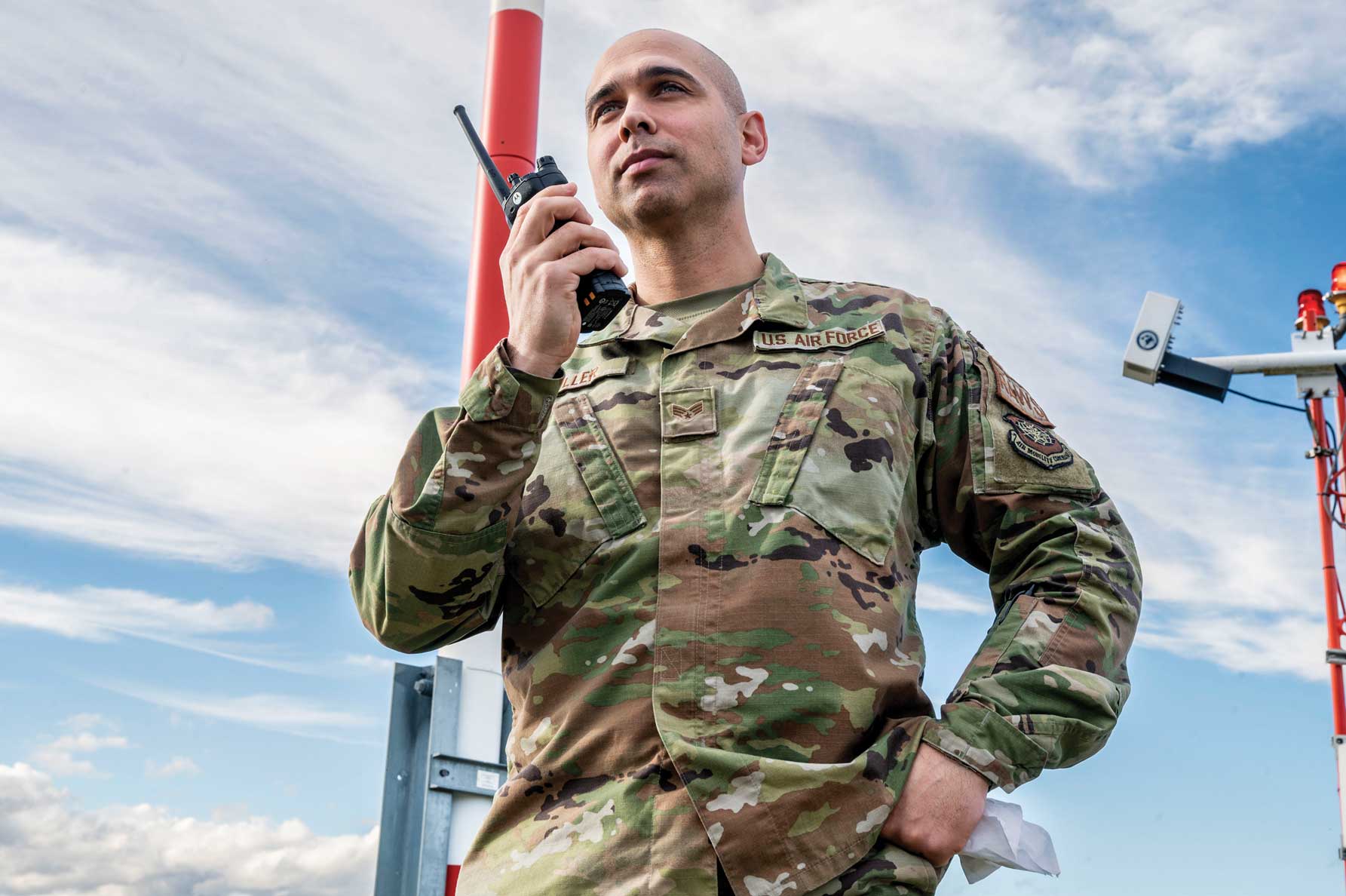 A man in camouflage holding a radio and looking up.