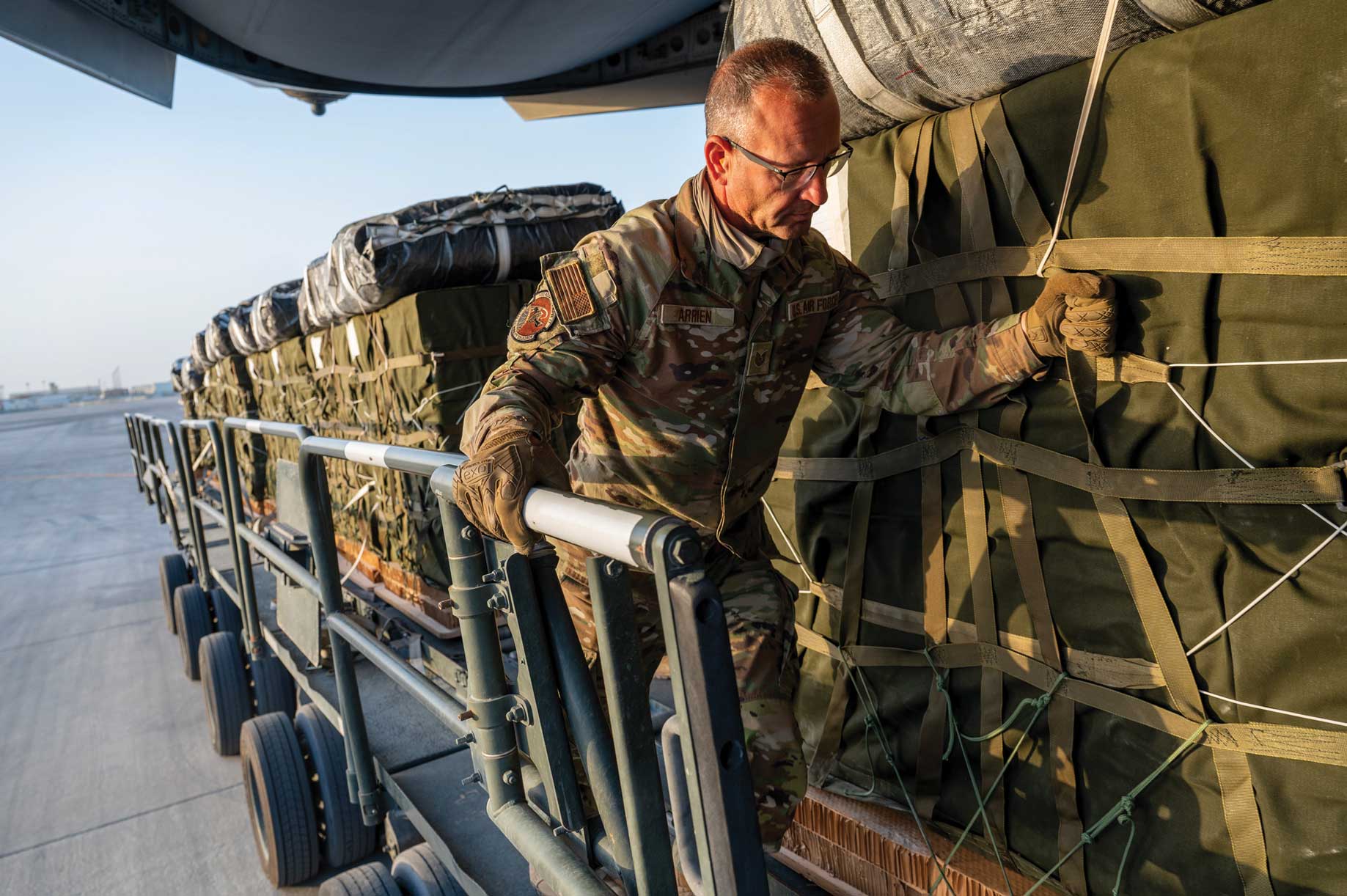 A man in camouflage is loading cargo onto a plane.