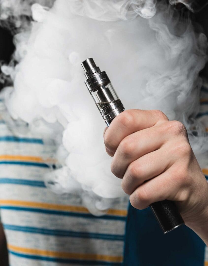 A person holding an electronic cigarette with smoke coming out of it.