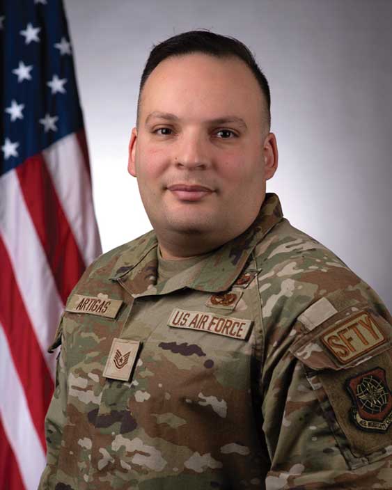 A man in military fatigues standing next to an american flag.