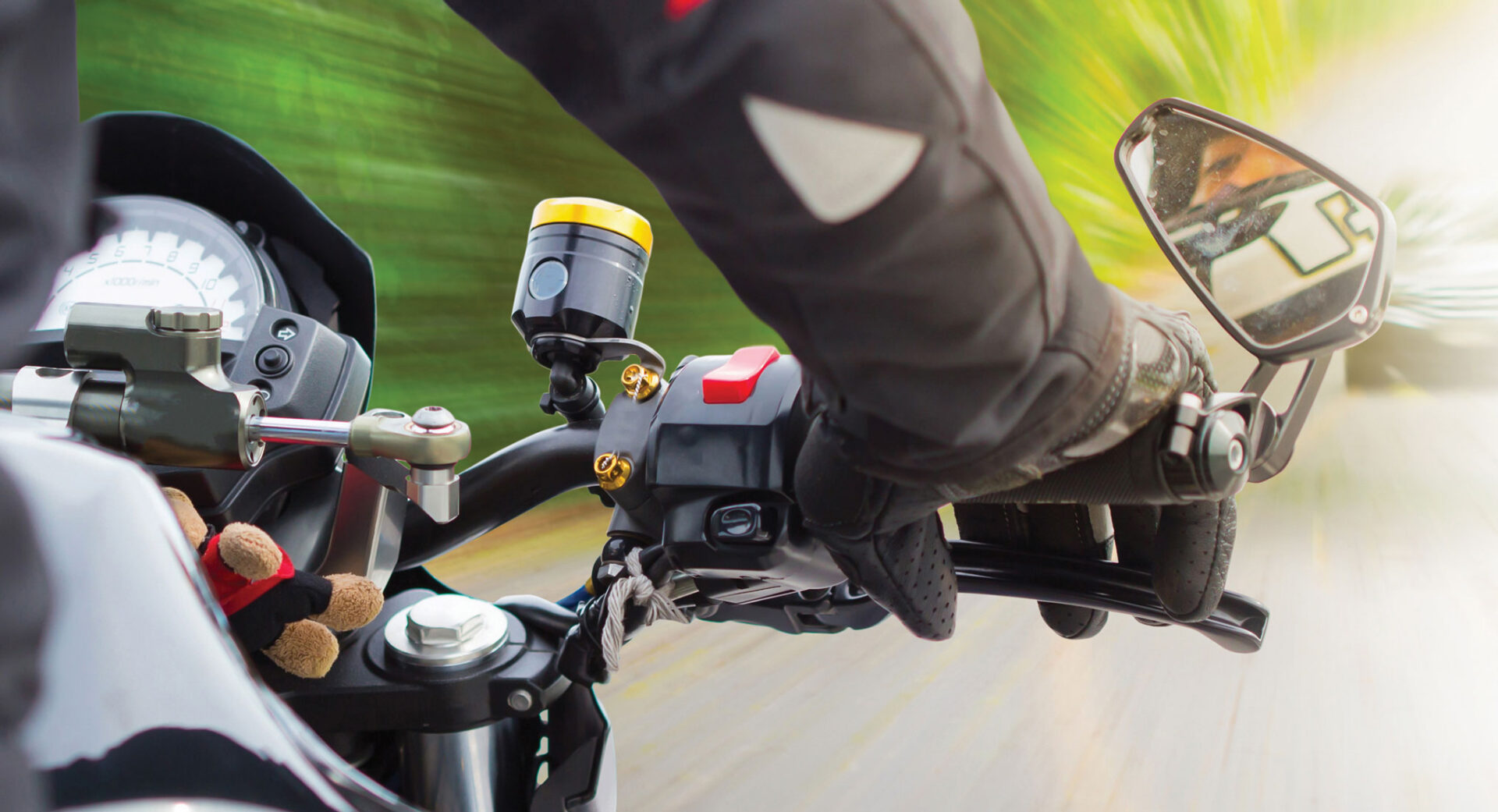 Close up view of a motorcycle rider's gloved right hand and the side mirror attached to the handlebar.