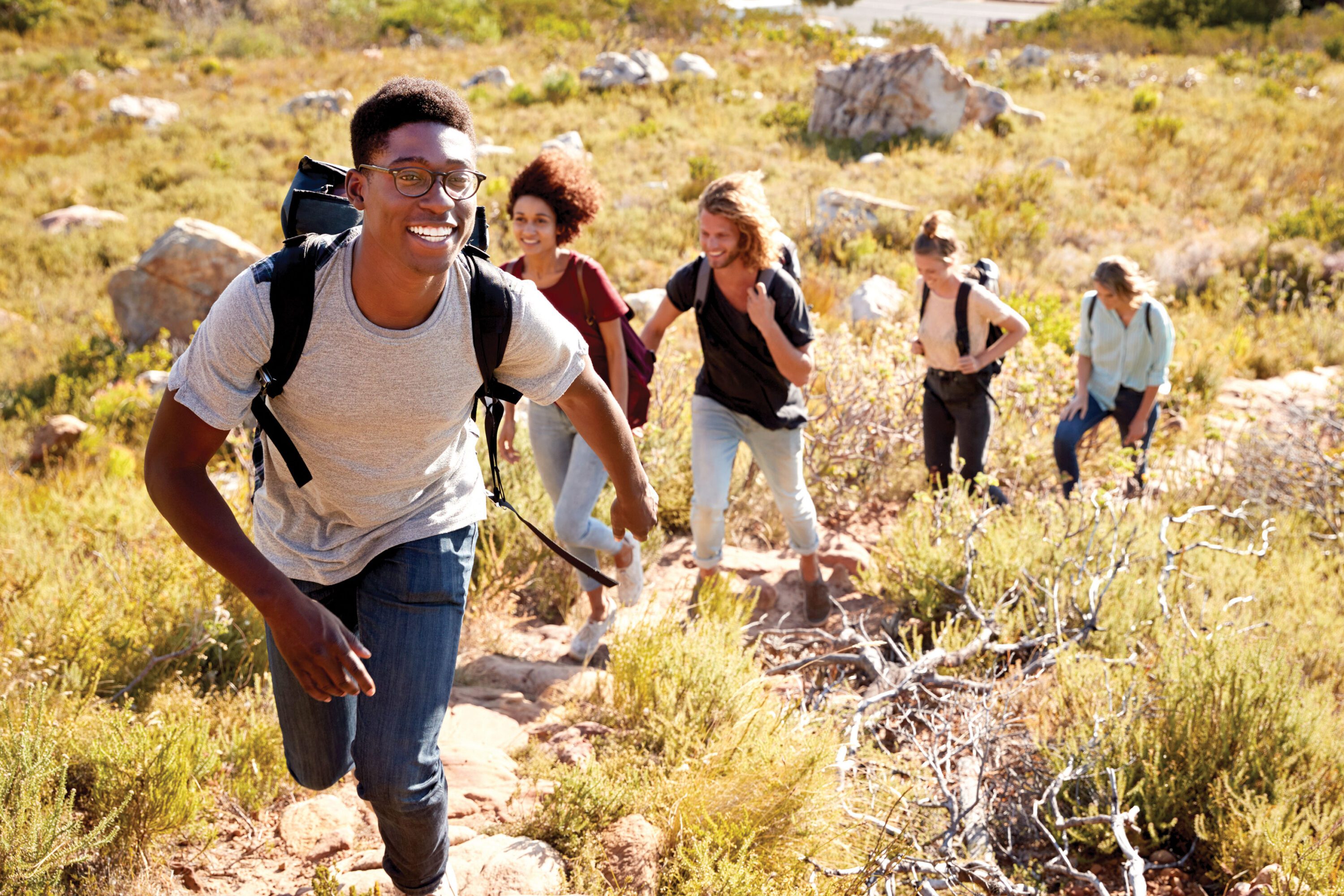 A group of five people with backpacks, hiking up a hill.