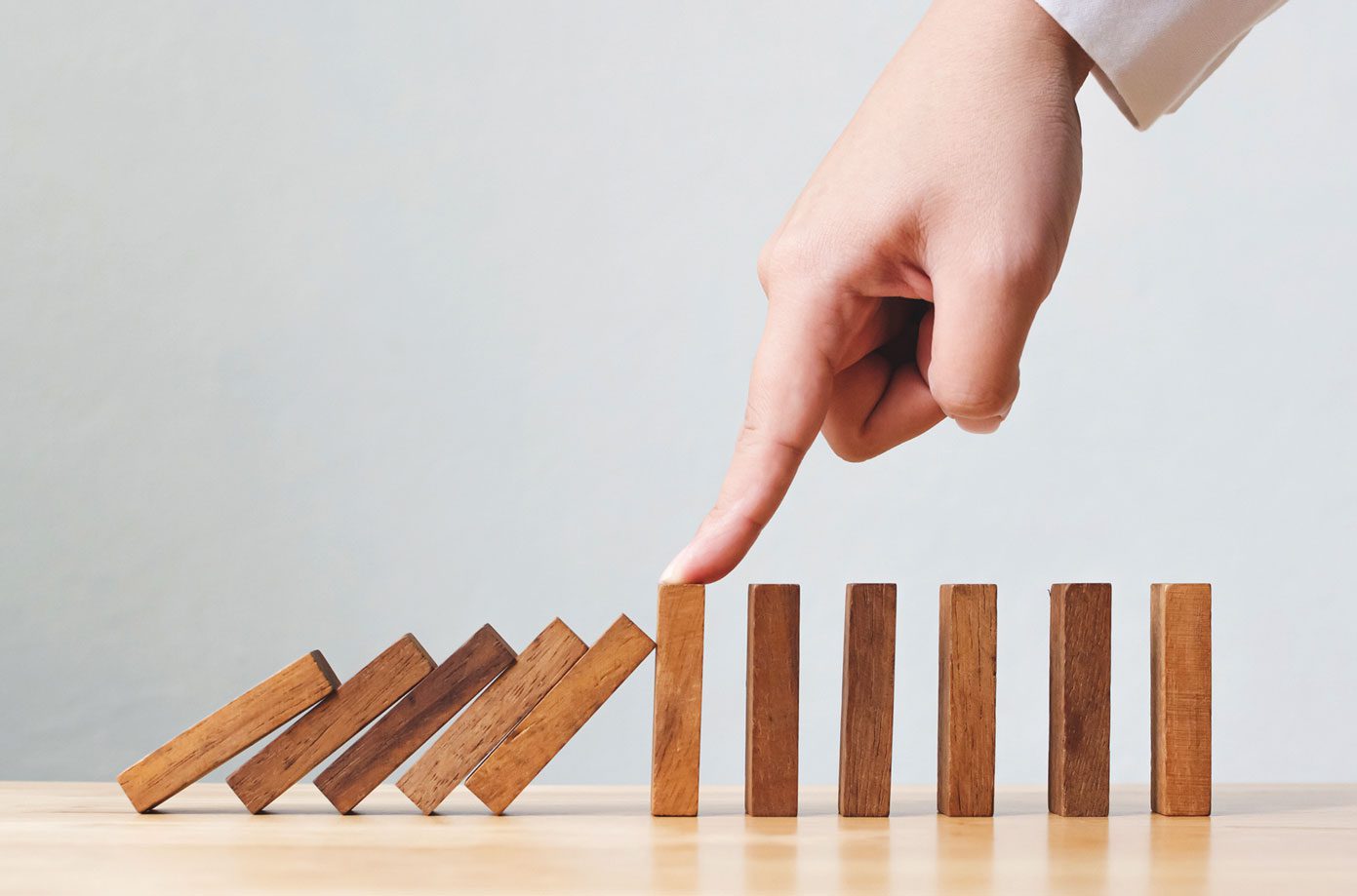 A row of wooden blocks falling to the right are stopped in the middle by a person's finger.