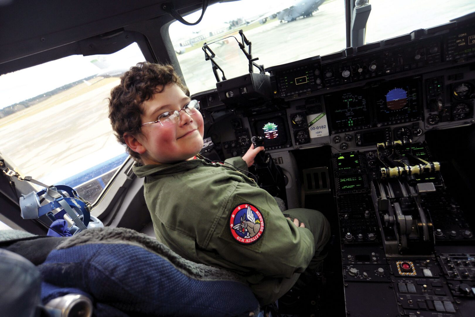 A young boy wearing a pilot uniform sits at the controls of an aircraft.