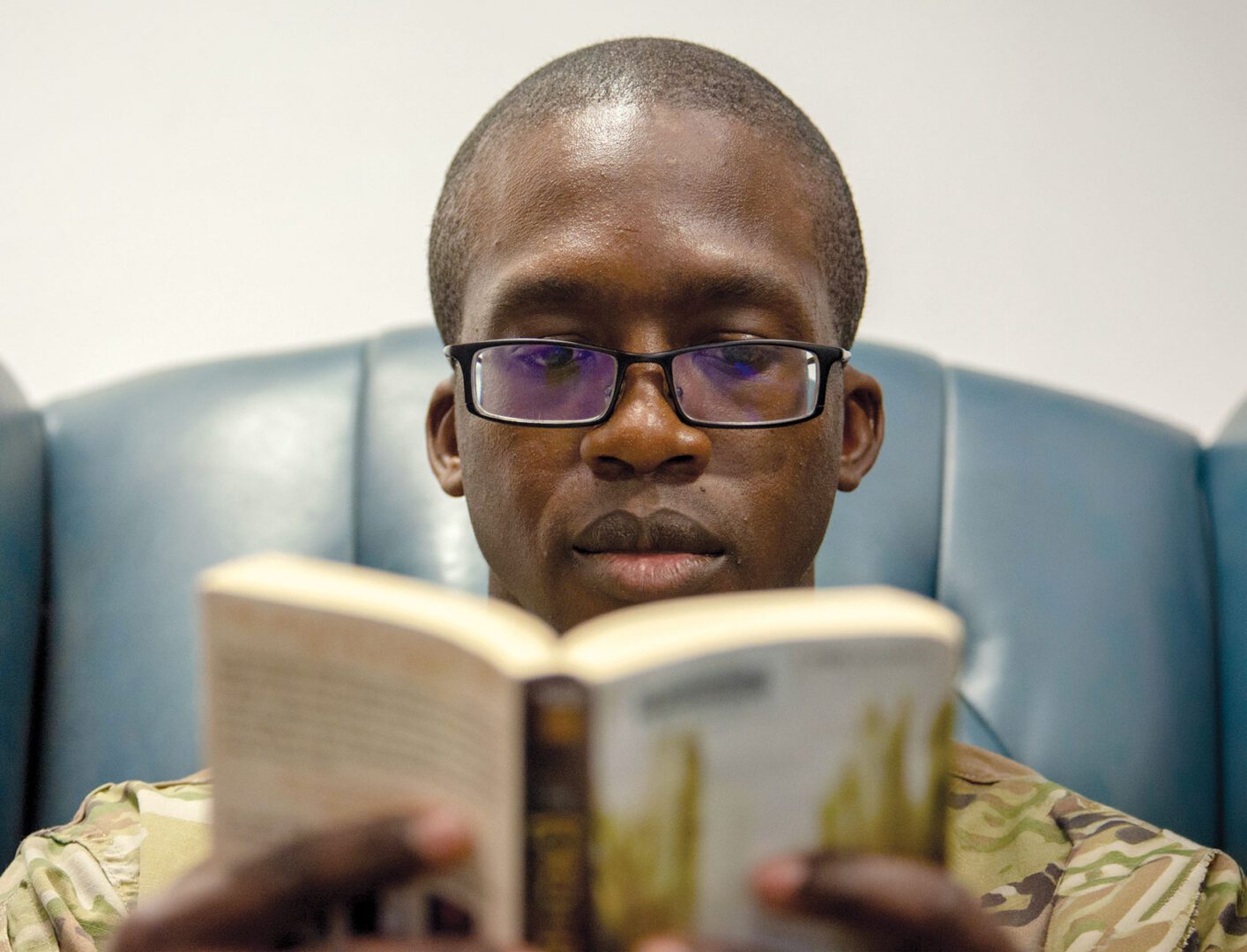 A man in an Air Force uniform sits in a chair reading a book.